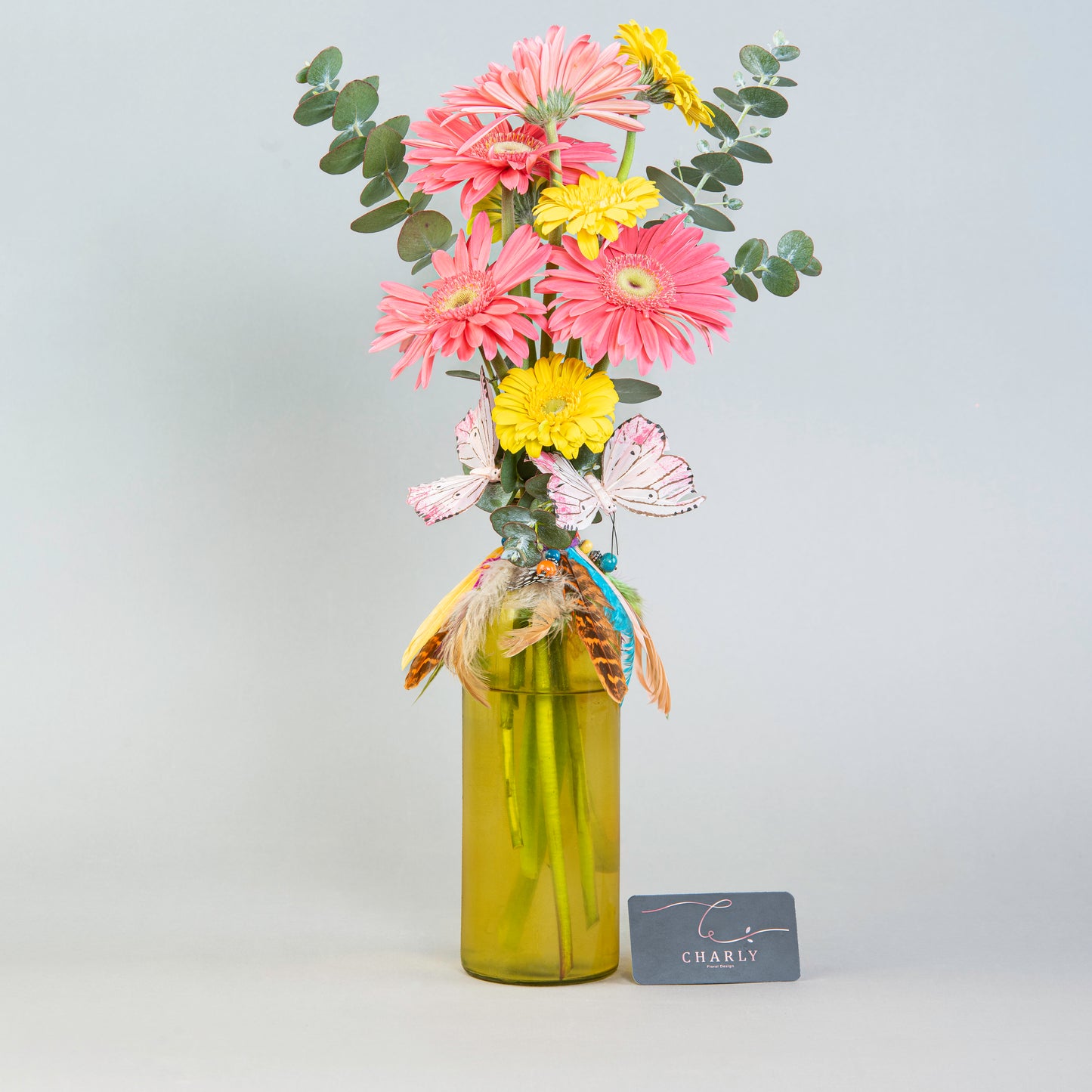 Sunshine Whimsy: Pink and Yellow Gerberas in Yellow Bottle with Feathers